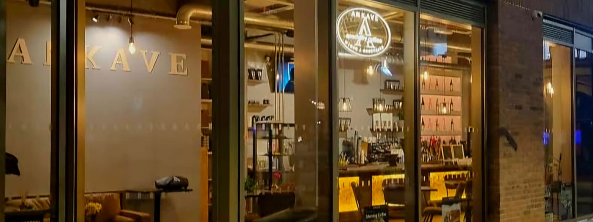 The night-time exterior of Ankave Coffee and Cocktails, Leeds, with the gold ANKAVE wordmark on the left window and the circular Ankave logo glowing through the warm-lit interior of the bar.