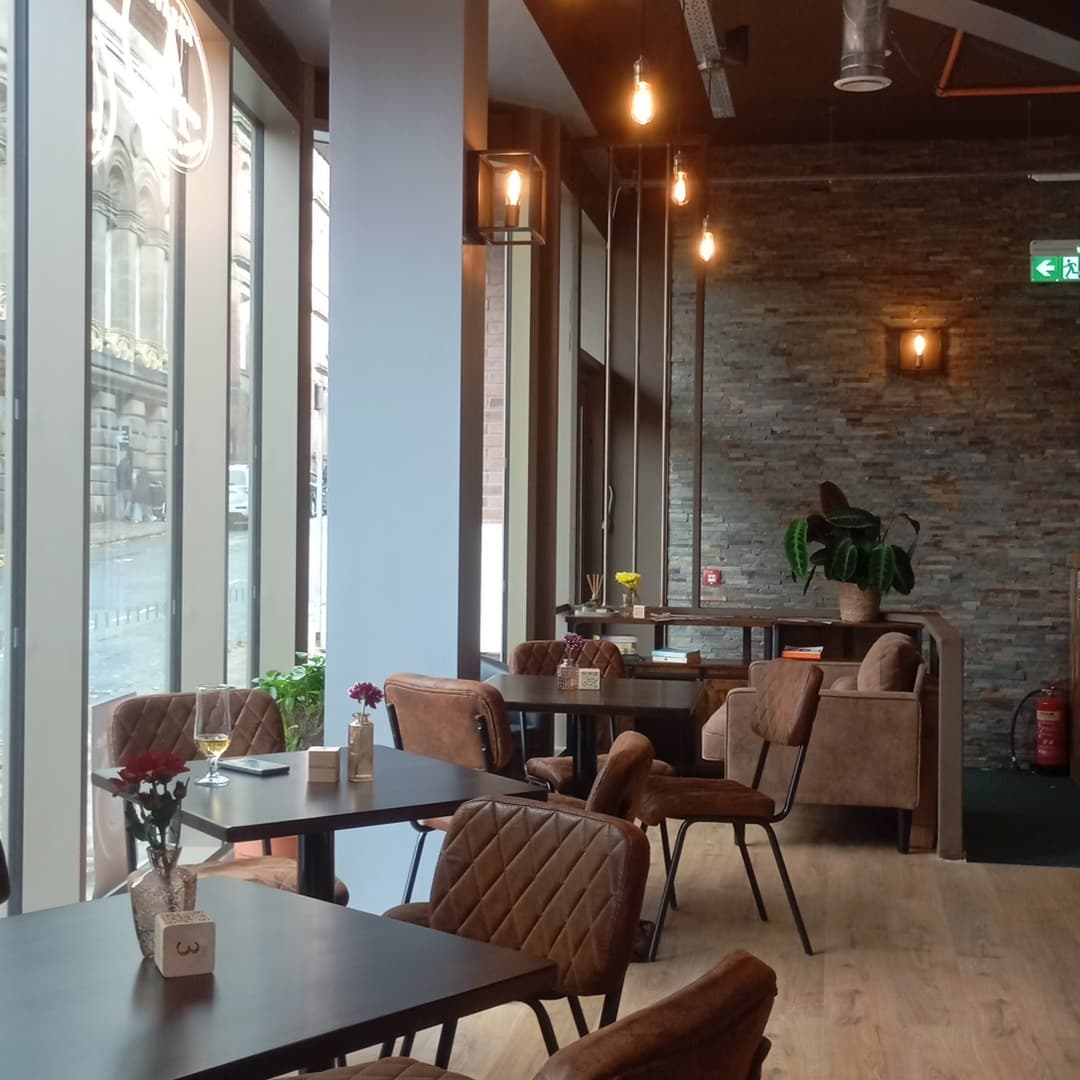 The interior of Ankave Coffee and Cocktails, Leeds, with diamond-stitched tan leather chairs, dark tables, exposed brick wall, and Edison bulb pendant lights.