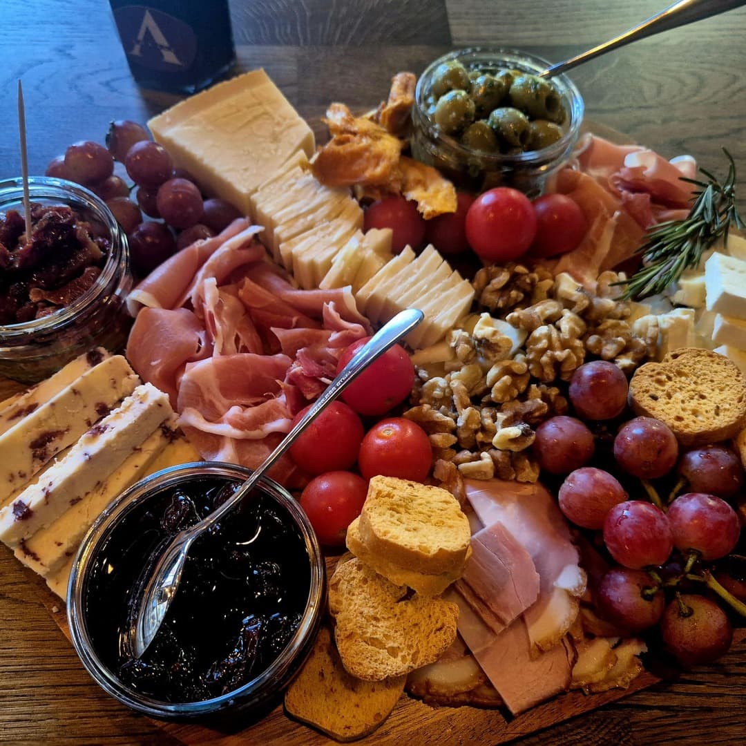 A charcuterie board at Ankave Coffee and Cocktails, Leeds, with cheeses, prosciutto, grapes, walnuts, olives, jam, crostini, and rosemary.