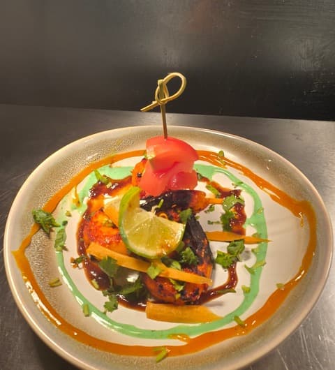 A tandoori chicken dish at Bombay Junction, Leeds, plated with tomato and lime garnish, sauce circles in green and orange, and matchstick carrots.