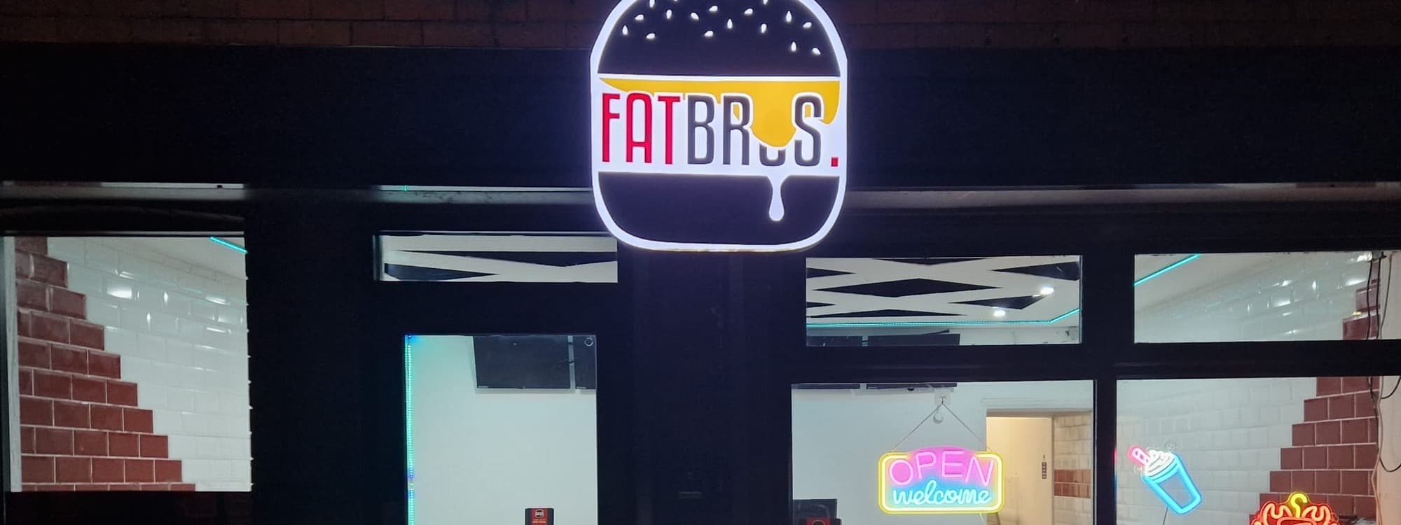 The illuminated FATBROS burger-shape logo on Hough Lane in Bramley, Leeds, with neon OPEN/welcome and burger, donut, fries and KEBAB signs visible in the window below.