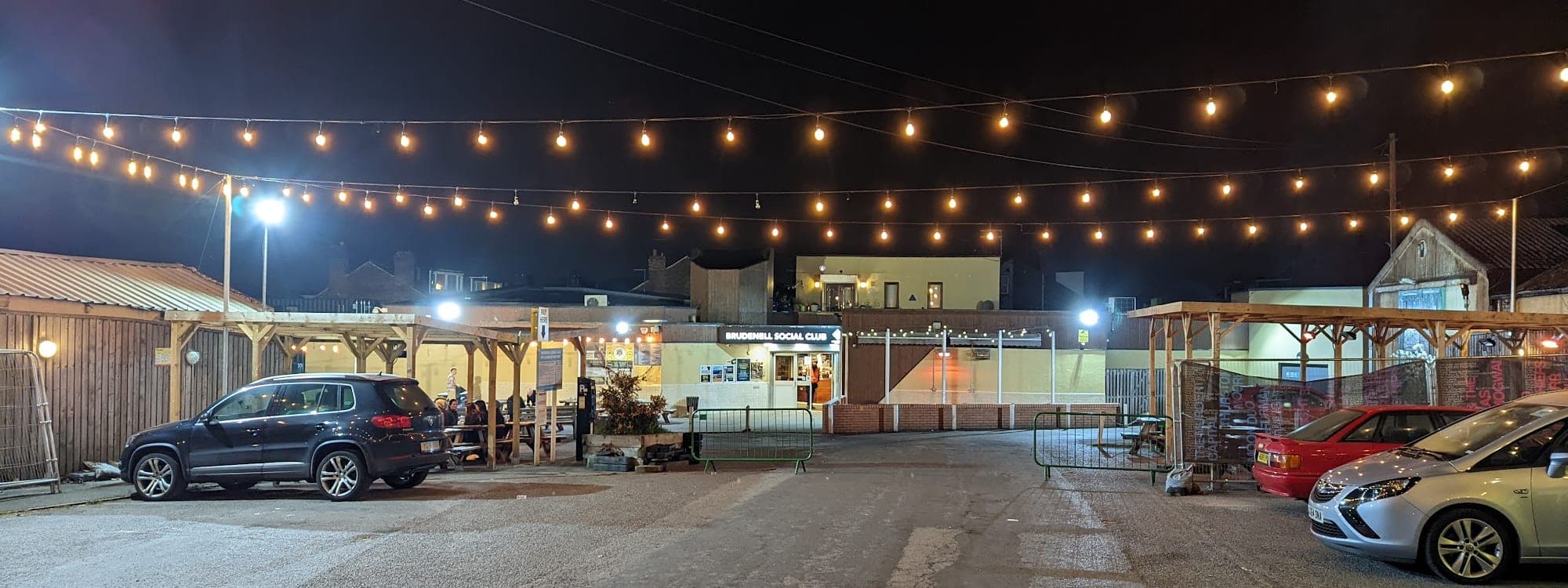 Outdoor courtyard at Brudenell Social Club Leeds at night, festoon lights strung above tables with the venue building beyond