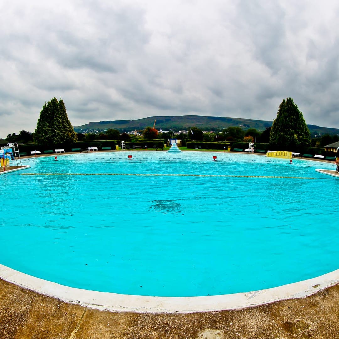 Ilkley Lido open-air pool with lawn, changing buildings and the edge of the moor.