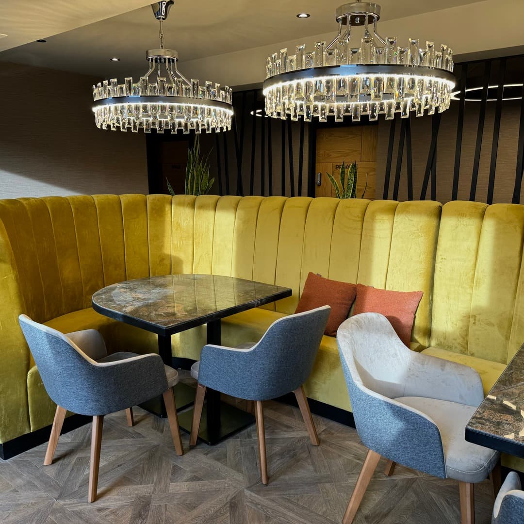 Yellow velvet curved banquettes with grey upholstered chairs, marble tables and ornate crystal-drop chandeliers in the dining room of Izgara Mediterranean Grill, Garforth, Leeds.