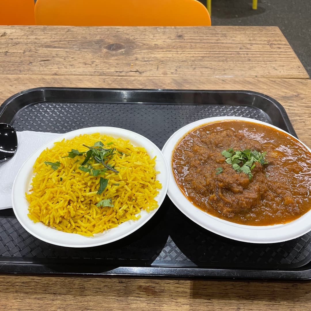 A bowl of yellow basmati rice with mint and a bowl of dark, slow-cooked curry topped with coriander, served on a black tray at Leziza, Leeds Kirkgate Market.
