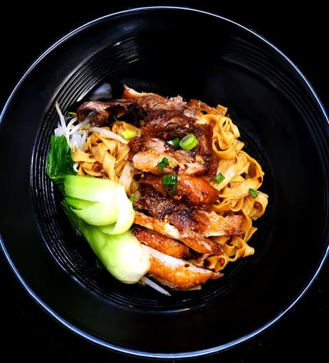 A black bowl of golden noodles topped with sliced beef and pak choi, served at Mr Su Noodles, Leeds.
