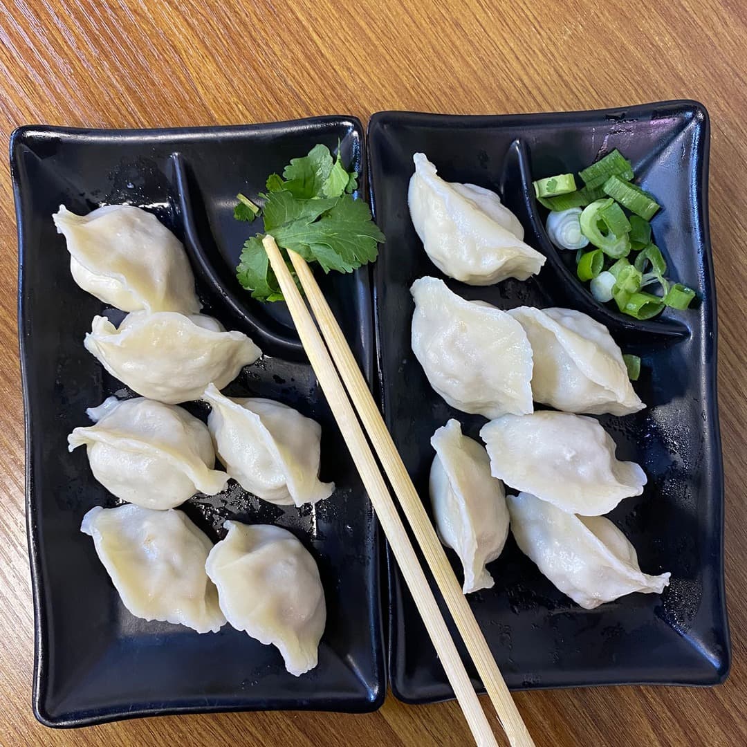 Two black plates of home-made dumplings at Mr Su Noodles, Leeds, served with chopsticks, fresh coriander, and chopped spring onions.