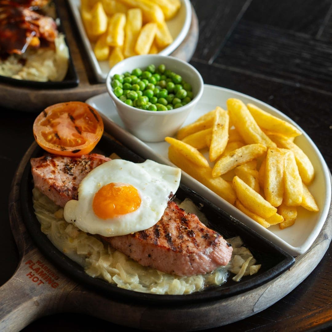 Sizzling steak on a cast iron pan with chips, fried egg, peas and tomato at The Roundhay in Leeds