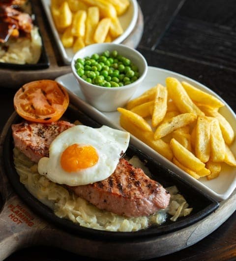 Sizzling steak on a cast iron pan with chips and peas at The Roundhay pub in Leeds