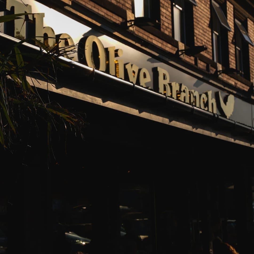 Exterior of The Olive Branch building with illuminated venue signage above the entrance on Street Lane Leeds