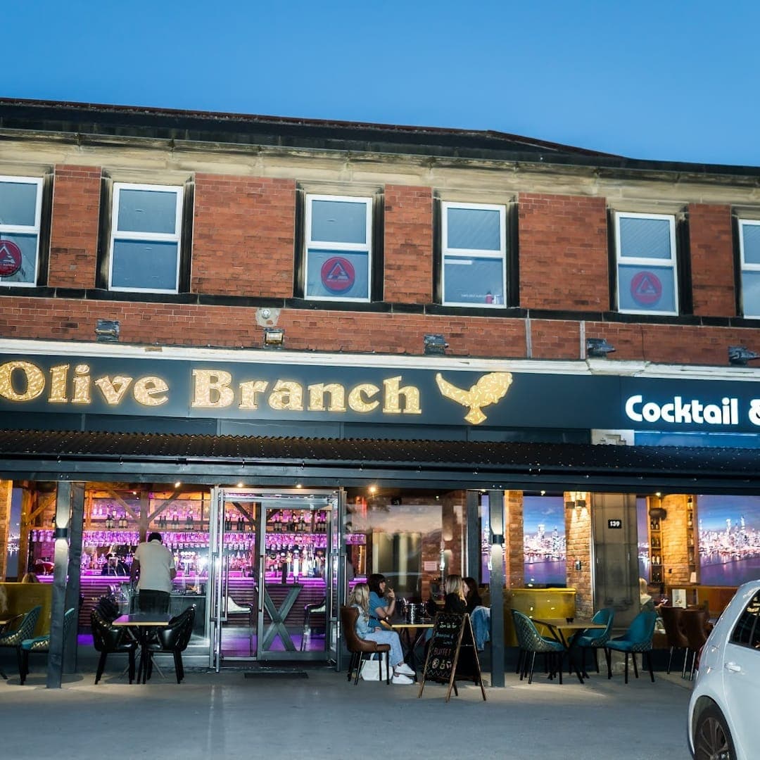 Evening exterior of TAPAS BAR by olive branch on Street Lane showing illuminated signage and outdoor seating