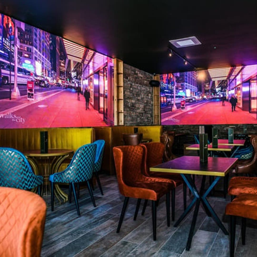 Interior of TAPAS BAR by olive branch showing large LED screen wall with vivid city nightscape and vibrant teal and orange seating