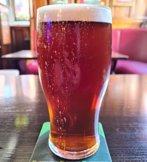 A pint of dark cask ale in a classic pub glass, served on a Greene King coaster in the Templar pub, Leeds.