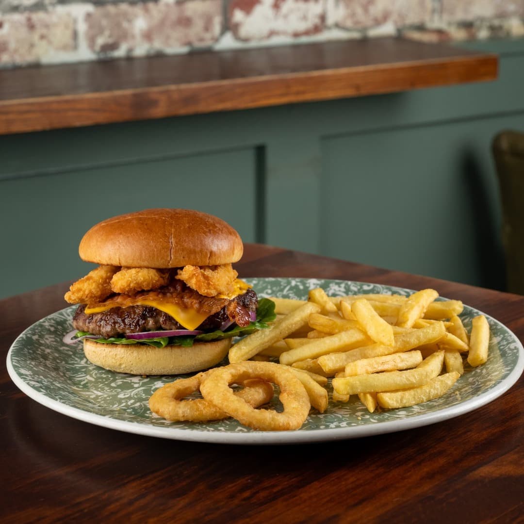 A beef burger with melted cheddar, onion rings and lettuce, served with chips and onion rings on a green-patterned plate at the Templar pub, Leeds.