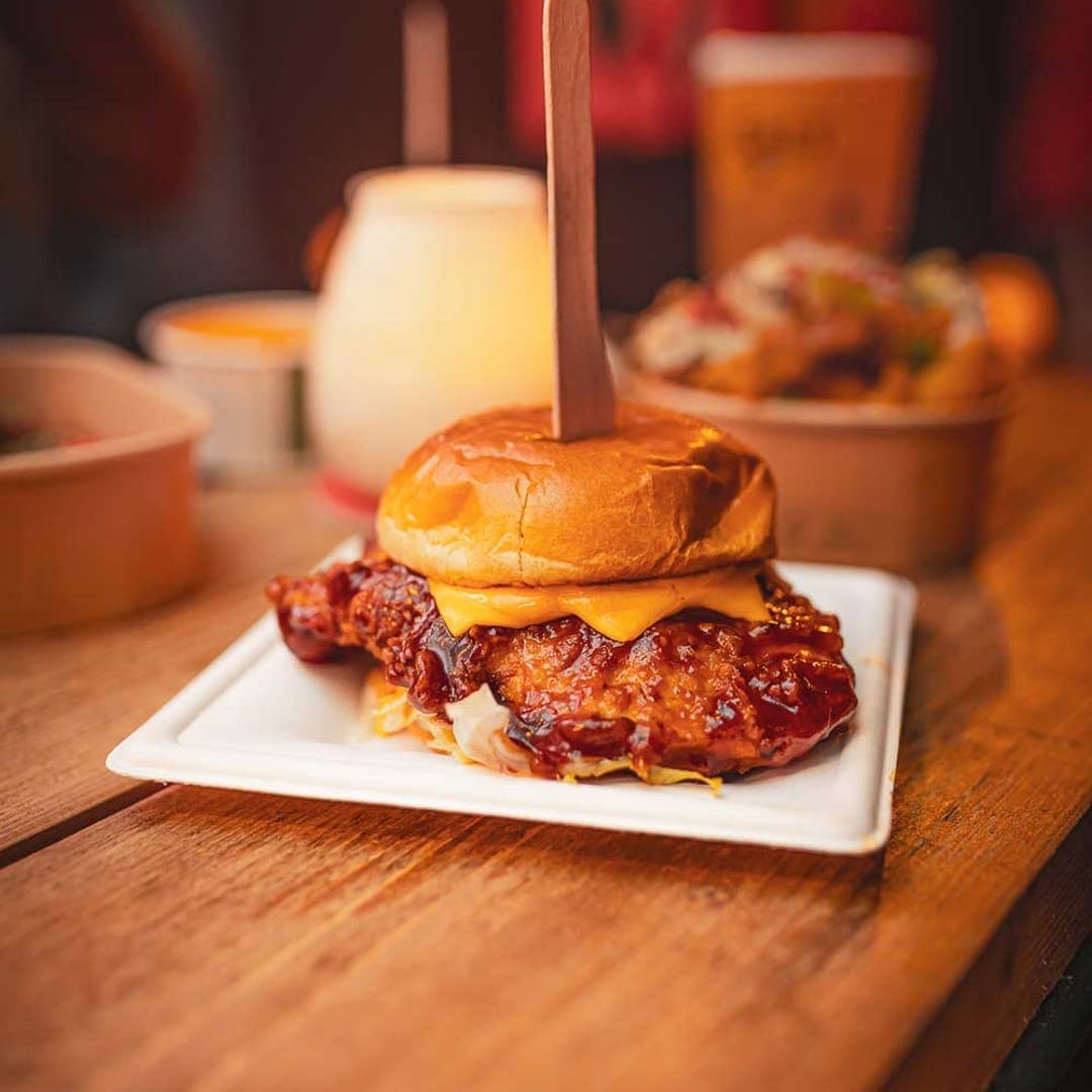 BBQ glazed fried chicken burger with melted cheese on a brioche bun, served on a white plate on a wooden table