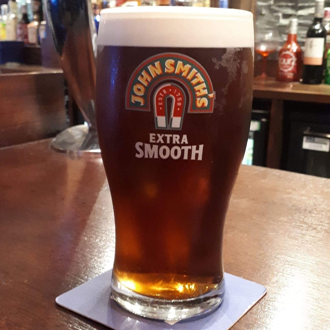 A pint of John Smith's on the bar at The Orchard with the venue sign lit up in the background