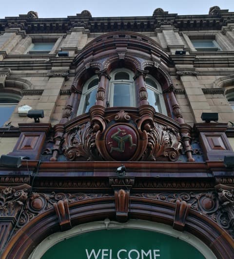 The carved triskelion medallion above the entrance arch of Three Legs pub on The Headrow, Leeds, with the green WELCOME sign below.