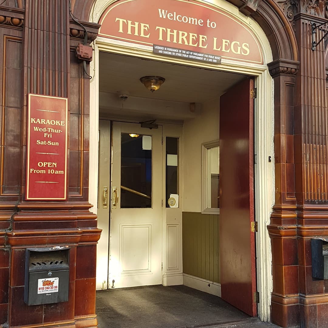 The recessed entrance of Three Legs pub on The Headrow, Leeds, with the burgundy and gold Welcome to The Three Legs sign above and the karaoke schedule on the left wall.