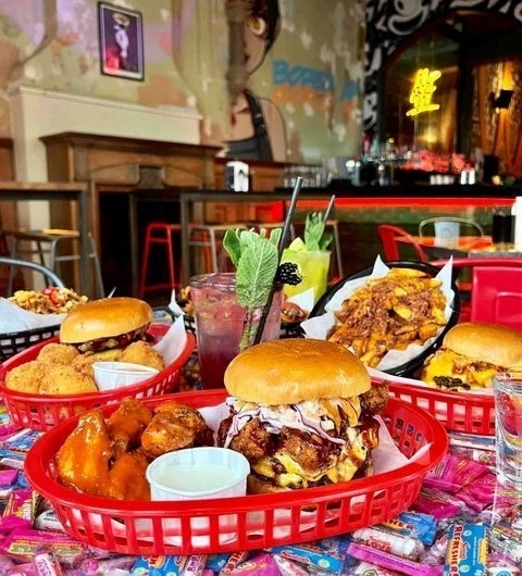 Almost Famous Delicious Burgers Wings Cocktails Delicious array of burgers, wings, and fries served in red baskets at Almost Famous, with refreshing cocktails and vibrant restaurant decor in the background.