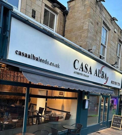 CasaAlba_ItalianRestaurantFacade_LeedsDining Exterior view of Casa Alba, an authentic Italian restaurant with a white and blue storefront, clear windows showcasing interior dining tables, and contact information displayed on the awning.