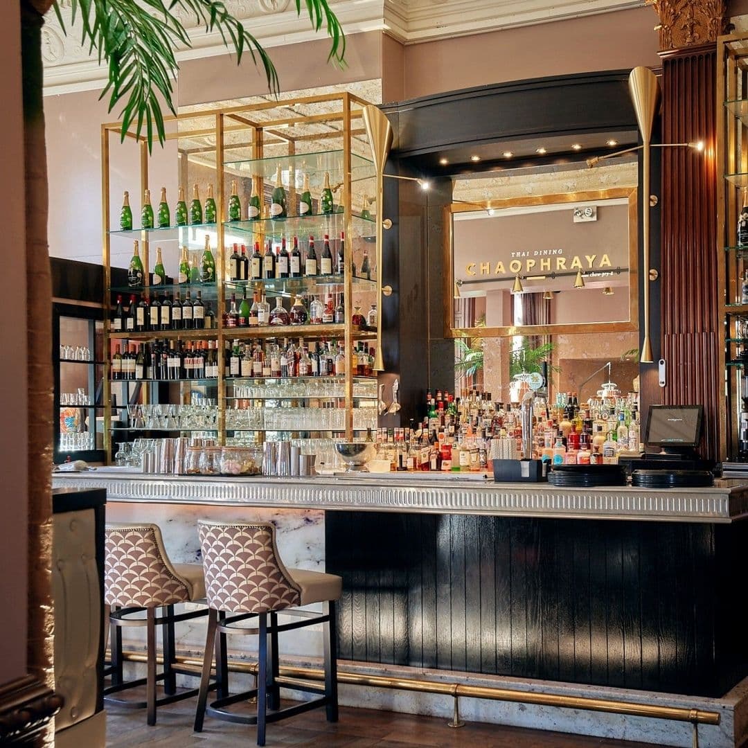 Elegant bar area at Chaophraya with a wide selection of bottles on glass shelves, marble countertop, and stylish bar stools.