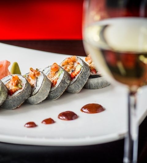 Chino Latino_Sushi Platter_White Wine_Elegant Dining Sushi rolls with toppings on a white plate, Chino Latino, with a glass of white wine in the background.