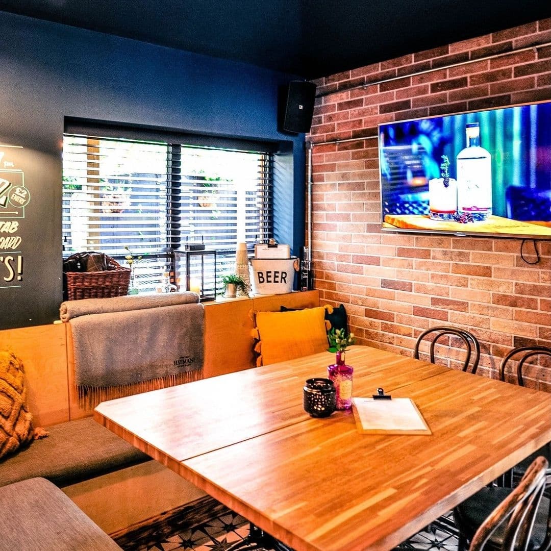 Cozy interior of Granvilles Beer & Gin House with wooden tables, comfortable seating, brick walls, and a television screen displaying a gin bottle.