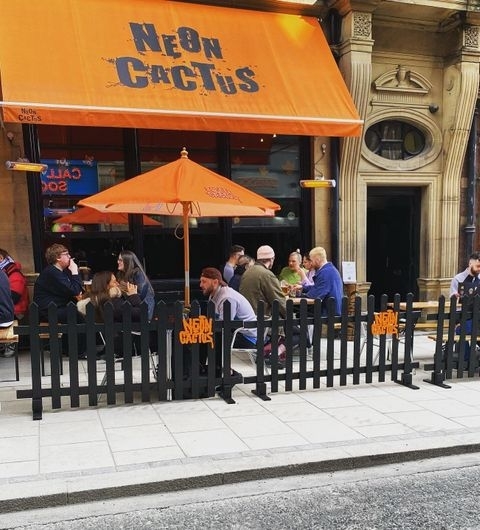Neon Cactus Outdoor Seating People Relaxing Outdoor seating area at Neon Cactus with patrons dining under an orange umbrella and a matching orange awning with the establishment's name.
