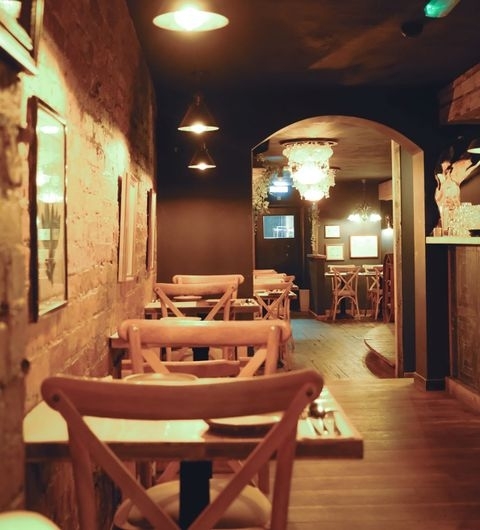 Phranakhon_Cozy_Restaurant_Interior_Warm_Lighting Cozy interior of a cafe with wooden chairs and tables, pendant lights, and exposed brick walls in Phranakhon.