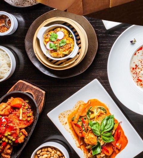 Sukhothai Chapel Allerton Thai Cuisine Dishes Top View Assorted Thai dishes from Sukhothai Chapel Allerton, featuring a bamboo steamer with dumplings, a plate of red curry, and other spicy specialties, garnished with fresh herbs.