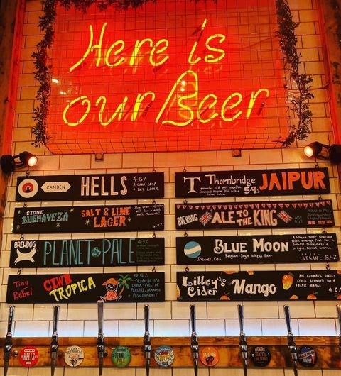 The Bowers Tap Neon Sign Craft Beer Selection Beer selection on tap at The Bower's Tap, featuring a variety of craft beers and ciders with neon sign reading "Here is our Beer" above the taps.