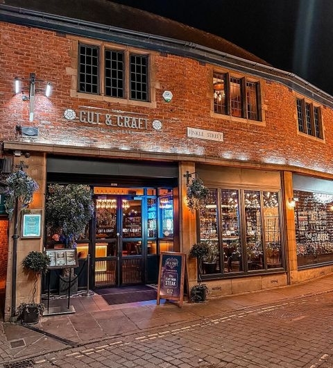 The Cut and Craft Steakhouse Evening Ambiance Exterior view of The Cut & Craft, a traditional brick building at night, illuminated by warm lighting with a visible entrance and windows displaying a cozy interior.