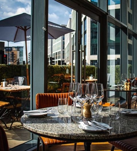 The Whitehall Restaurant Bar Upscale Dining Patio View Elegant dining setup at The Whitehall Restaurant & Bar with wine glasses on a marble table, plush seating, and a view of the cityscape.