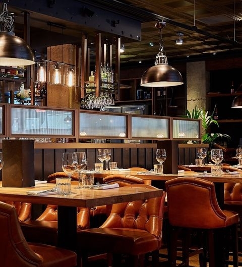 Blackhouse_Elegant_Dining_Ambiance_Leather_Seating Interior of Blackhouse restaurant featuring elegant leather seating, polished wooden tables set with wine glasses, and warm ambient lighting.