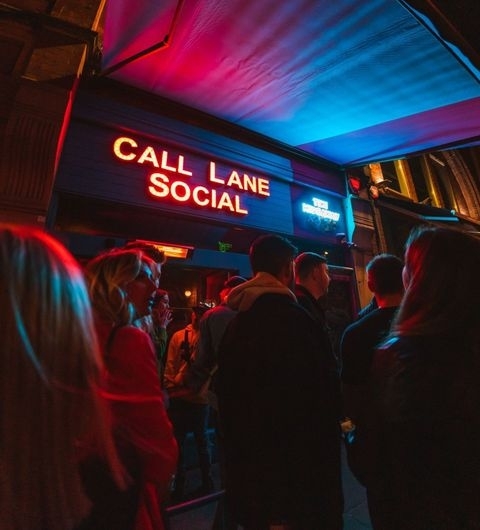 Call Lane Social Nightlife Neon Sign Crowd Crowd of people waiting outside the Call Lane Social bar under a glowing red neon sign at night.