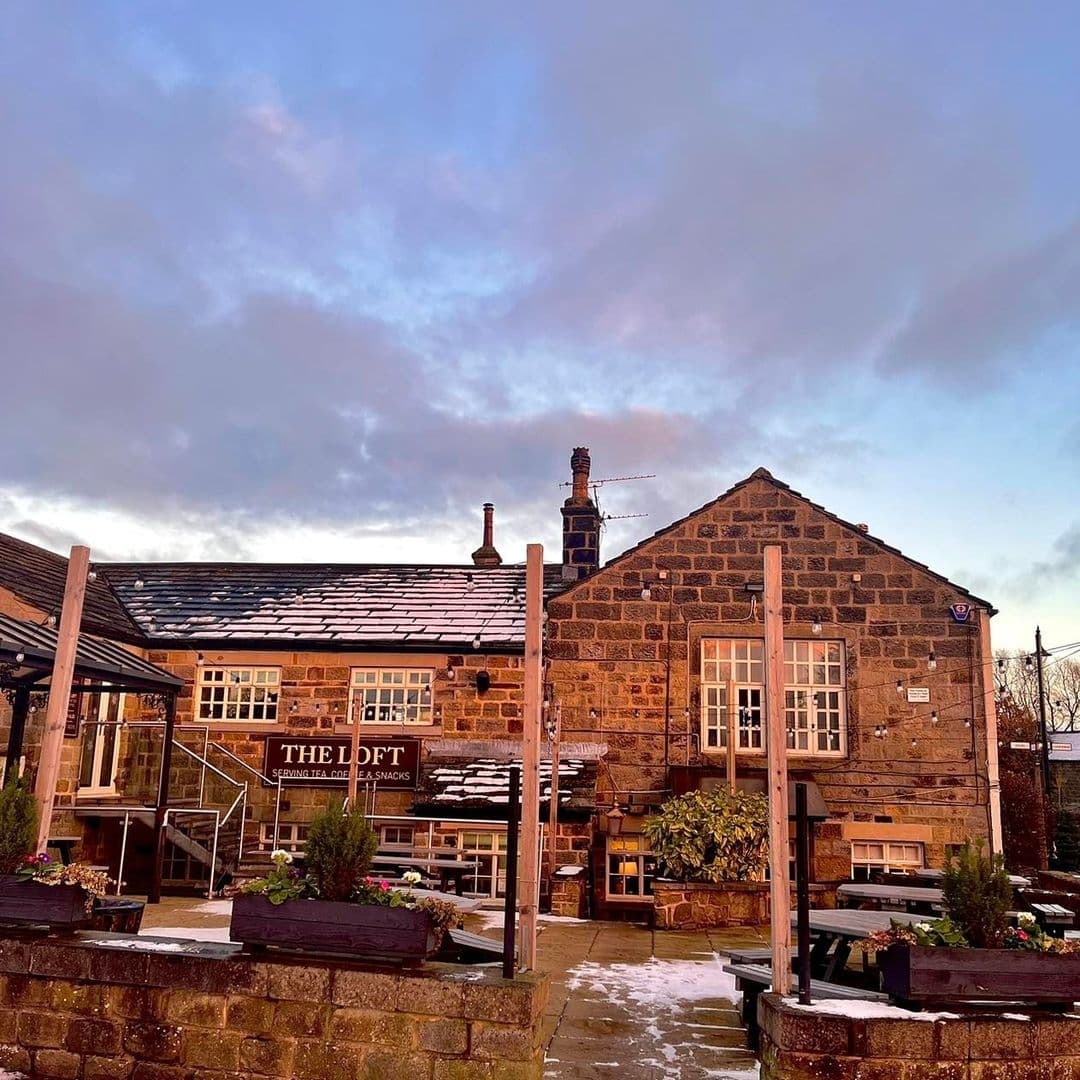Exterior view of Fox & Hounds with a stone building, a sign reading "THE LOFT," snow-dusted outdoor seating, and a twilight sky.