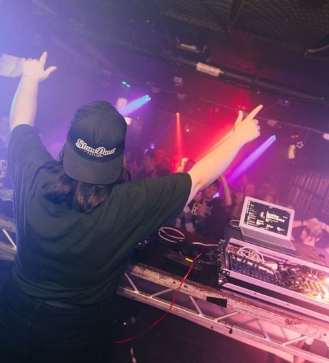 The Key Club_Nightlife_DJ_Performance_Crowd_Energy DJ performing at The Key Club with hands up and colorful stage lights in the background.