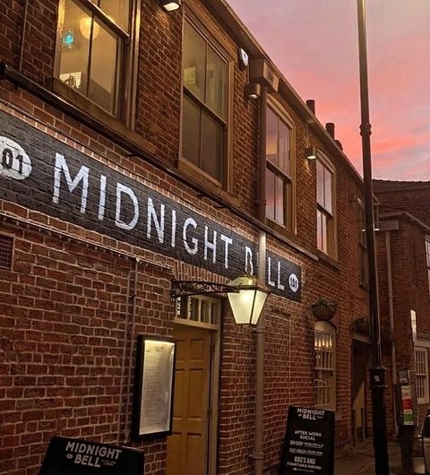 The Midnight Bell Pub Sunset Facade Sign Exterior of The Midnight Bell pub with illuminated signage on a brick facade at dusk.