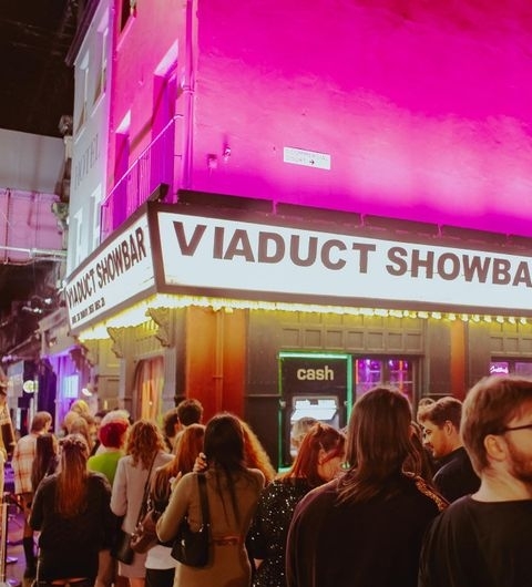 Viaduct_Showbar_Nightlife_Crowd_Purple_Lighting Crowd of people outside Viaduct Showbar at night with vibrant pink lighting on the building's facade.