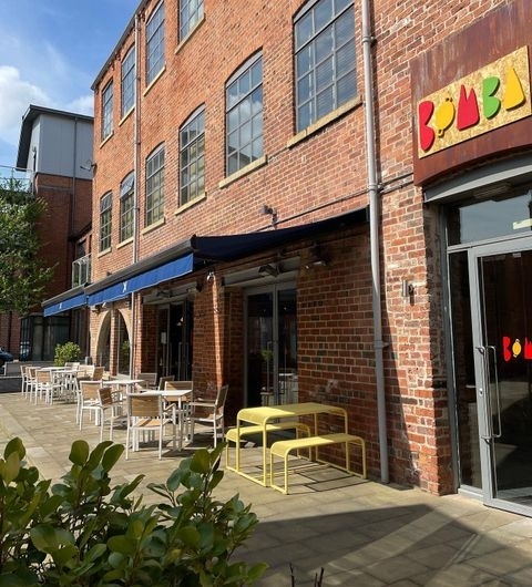 Bomba Paella Restaurant Exterior Sunny Patio Exterior view of Bomba Paella restaurant with outdoor seating, red brick facade, and colorful signage.