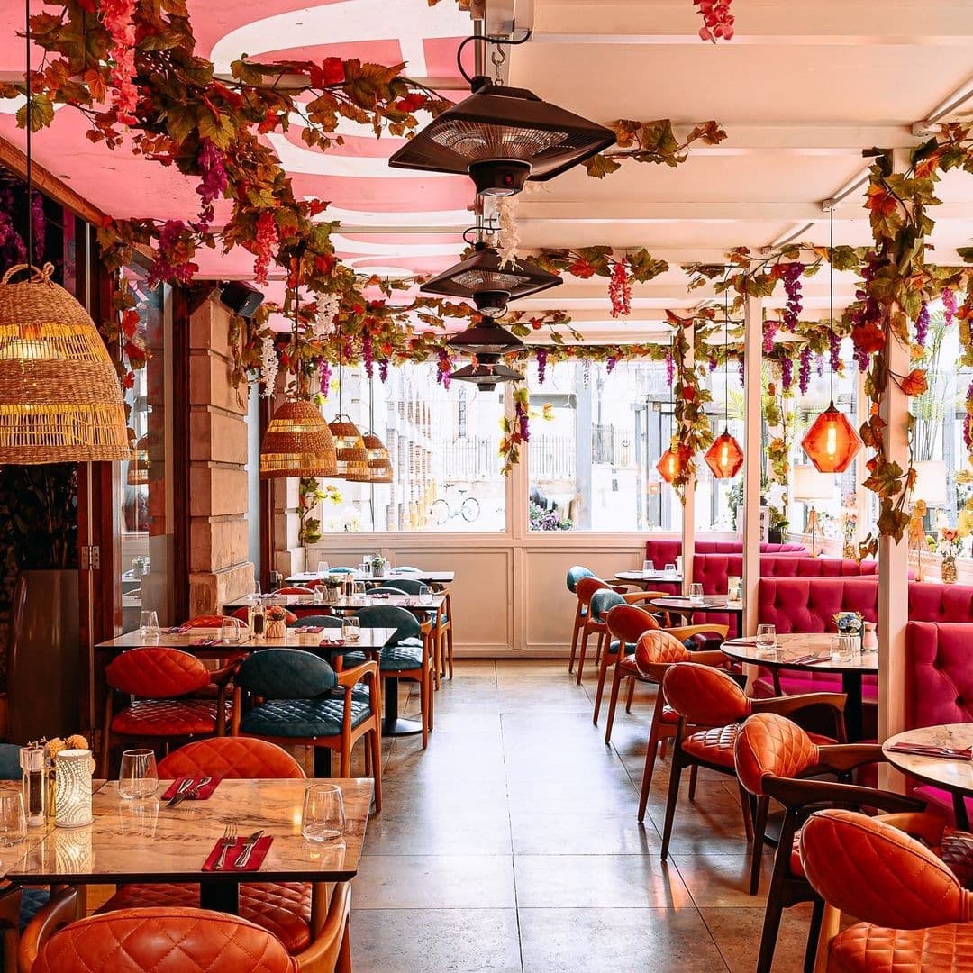Interior of Fleur Restaurant and Bar featuring elegant dining setup with colorful chairs, pink and red floral decorations, and stylish hanging lights.