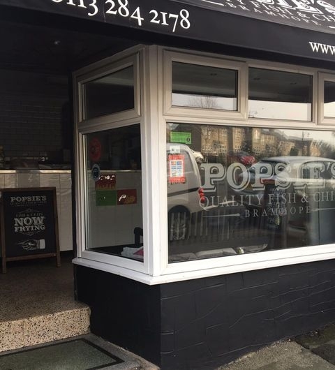 Popsies_of_Bramhope_Fish_and_Chips_Shop_Front Exterior view of Popsies of Bramhope, a fish and chips shop, with a black facade, white window frames, and a visible signboard.