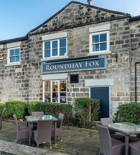 The Roundhay Fox Stone Building Outdoor Seating Exterior view of The Roundhay Fox, a traditional stone building with a sign above the entrance, outdoor seating available in the foreground.