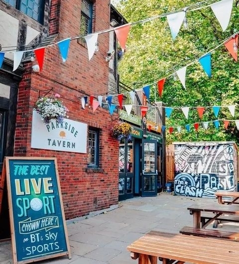 Parkside Tavern Outdoor Seating Festive Bunting Street Art Exterior of Parkside Tavern with colorful bunting, a chalkboard advertising live sports, and outdoor seating.