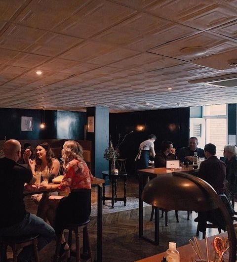 Below Stairs Cozy Social Scene Casual Dining Alt text: "Cozy ambiance at Below Stairs with groups of people seated at tables, engaging in conversation, in a dimly lit room with stylish decor."