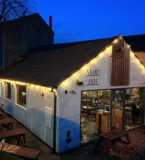 Saint Jude Twilight Cafe Exterior Warm Lights Exterior view of Saint Jude at dusk with warm lighting, featuring the building's white facade, string lights, and outdoor seating area.