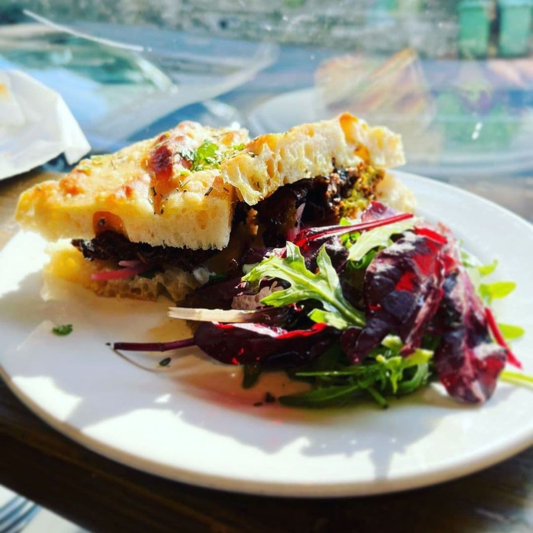 Gourmet sandwich with melted cheese and a side salad on a white plate at Mill Kitchen & Bakery.
