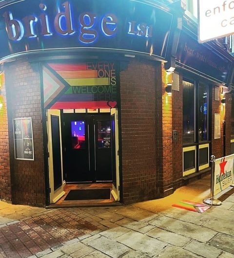 The Bridge Bar Neon Sign Welcoming Entrance Nighttime Exterior view of The Bridge Bar at night with illuminated signage, a welcoming entrance featuring a rainbow design and the text "EVERYONE IS WELCOME," and a Heineken sidewalk sign.