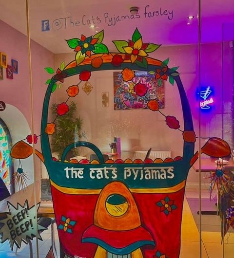 The Cats Pyjamas Farsley Colorful Rickshaw Artwork Entrance Colorful artwork of a tuk-tuk with floral designs and "The Cat's Pyjamas" written on it, displayed at The Cat’s Pyjamas – Farsley.
