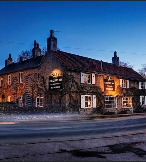 The Chequers Inn twilight ivy covered building historic pub Twilight view of The Chequers Inn, a traditional English pub with illuminated signage, nestled in a quaint building covered with ivy.